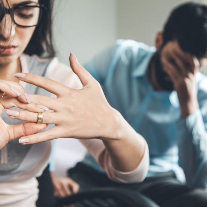 Eine Frau zieht ihren Ring vom Finger, im Hintergrund ein verzweifelter Mann.