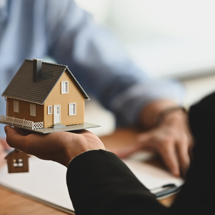 Makler hält ein Musterhaus in der Hand, Symbol für Rezession bei Immobilien