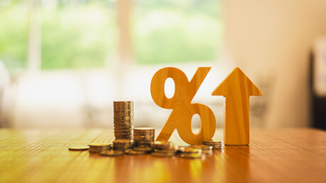 Münzen liegen neben einem Prozentzeichen. Neben dem Zeichen befindet sich ein Pfeil, der nach oben deutet.