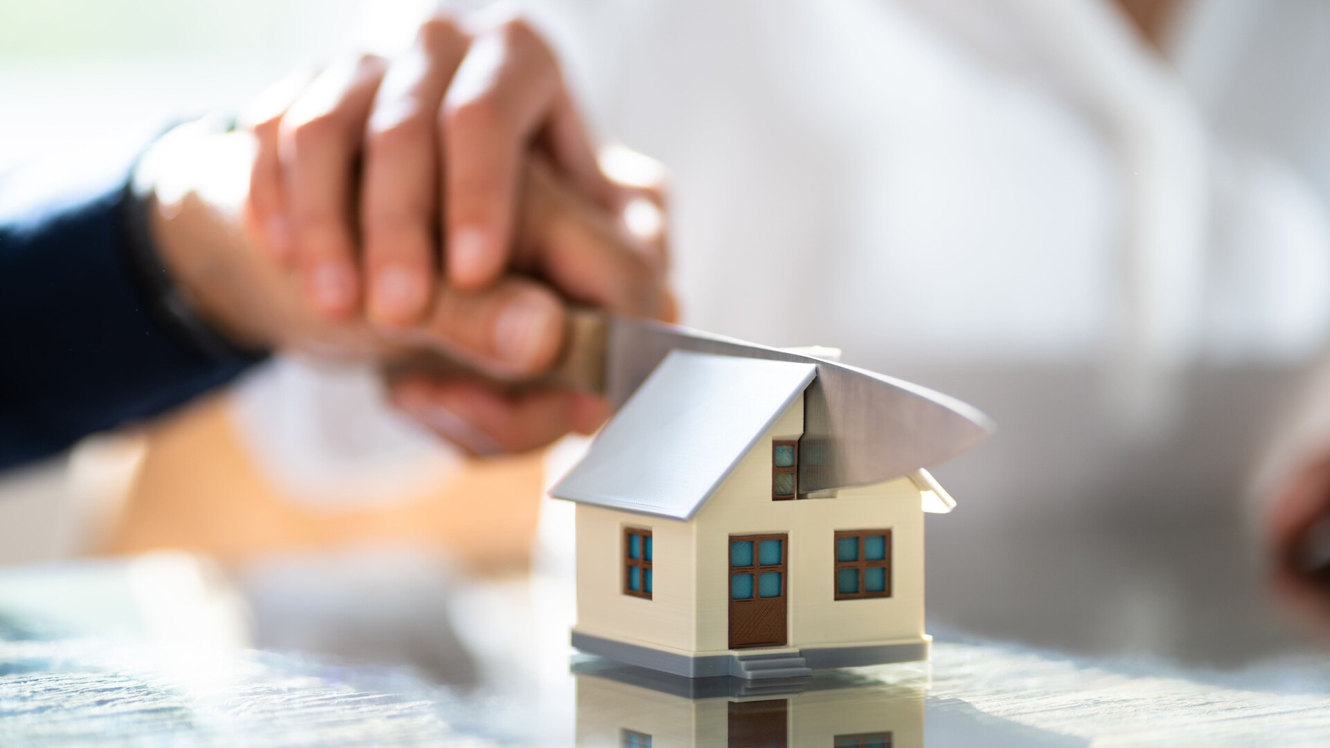 Ein Messer durchschneidet ein Modellhaus: Immobilie im Trennungsfall