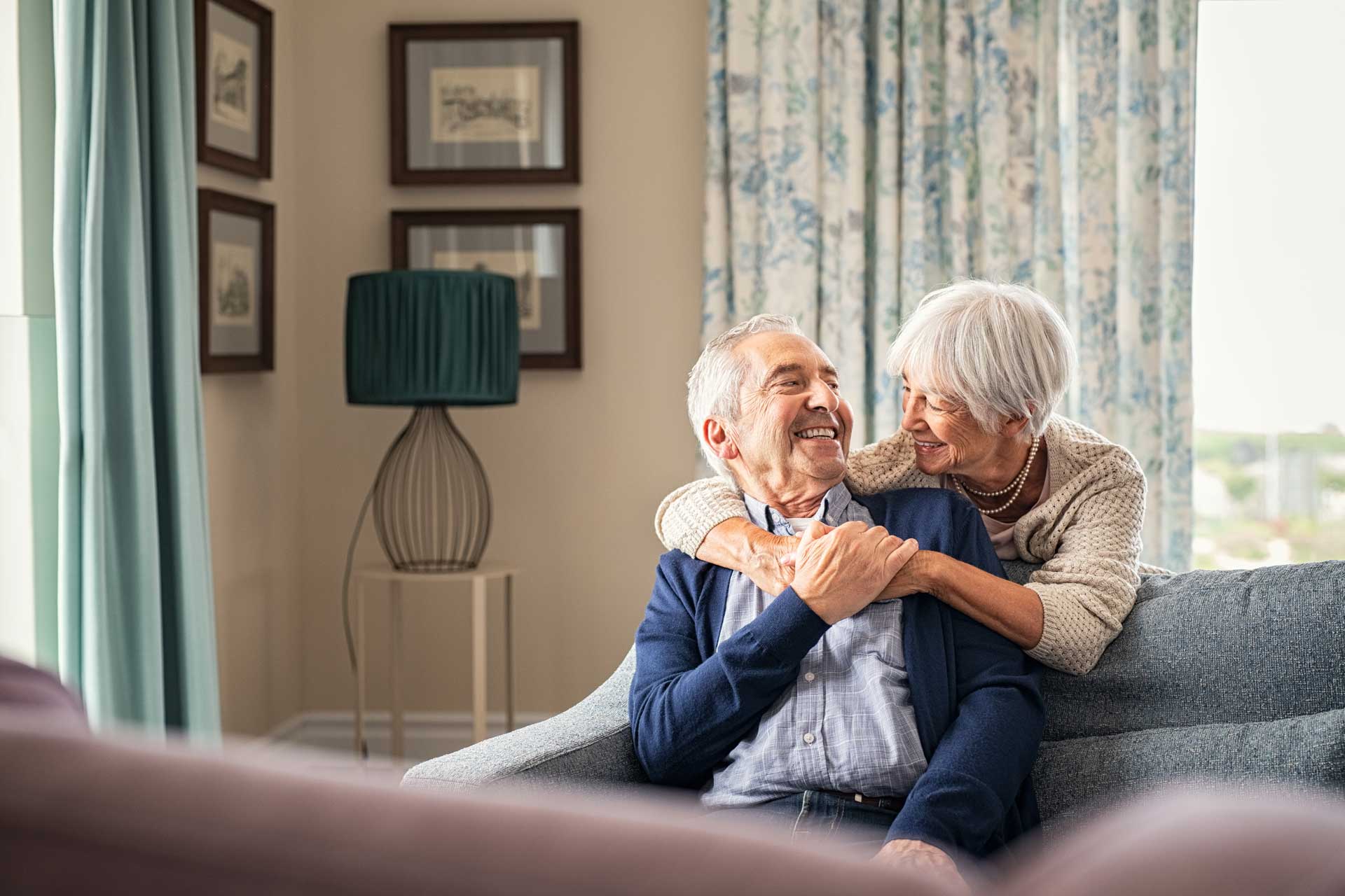 Seniorin umarmt ihren Ehemann im Wohnzimmer: Immobilienfit im Alter
