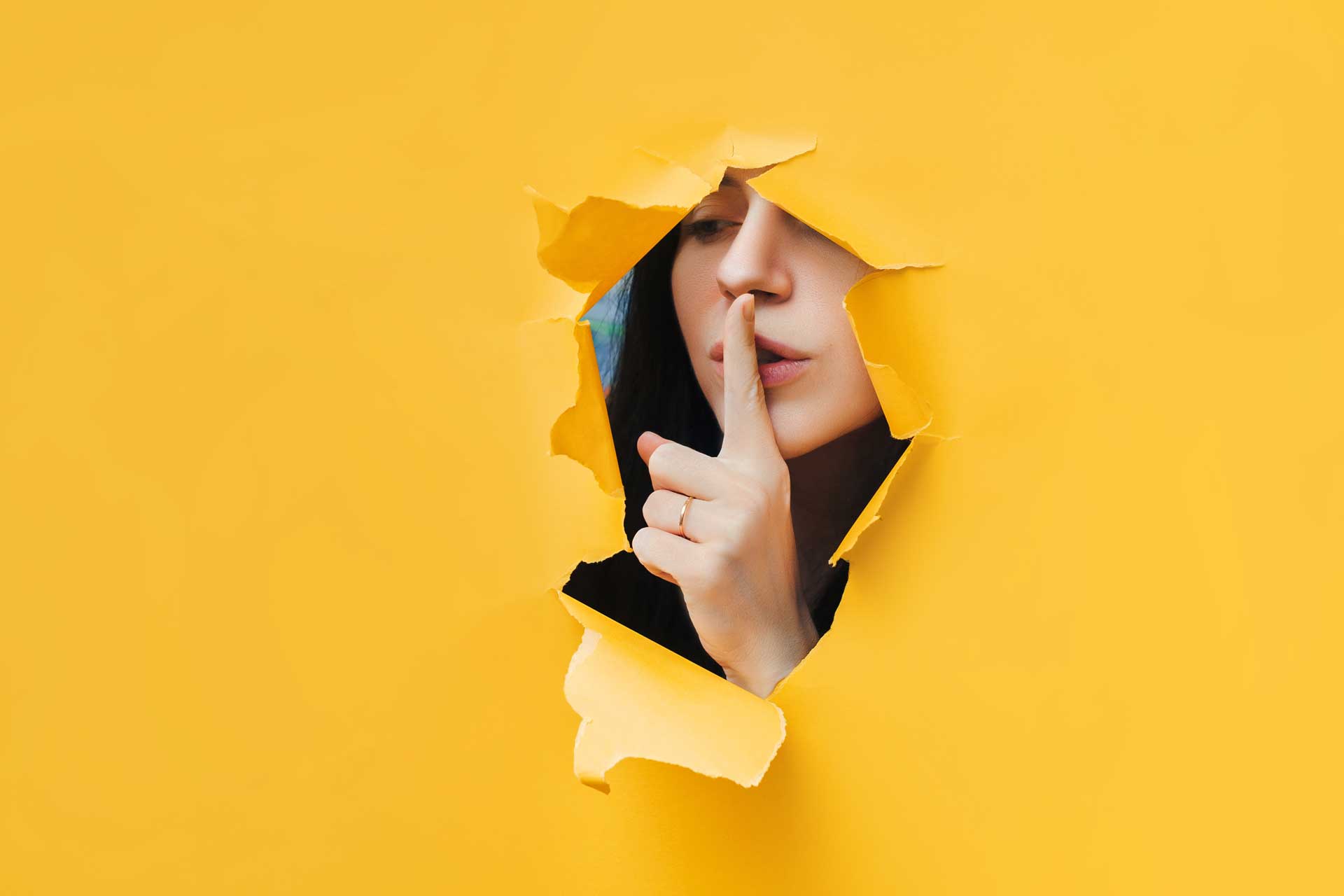 Junge Frau blickt durch Papier und hält den Finger vor den Mund: Secret Sale