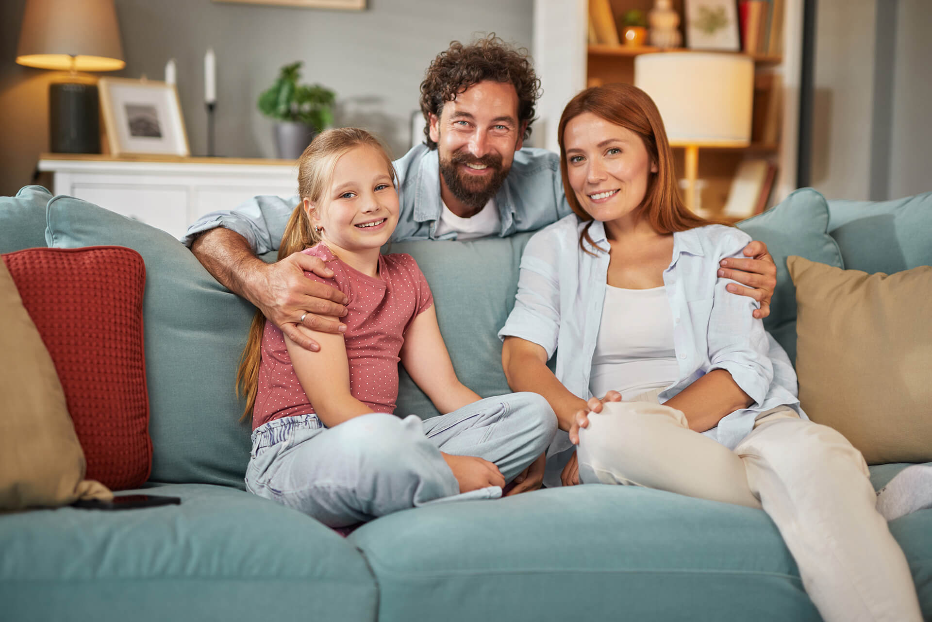 Familie zu dritt auf blauem Sofa im gemütlichen Wohnzimmer