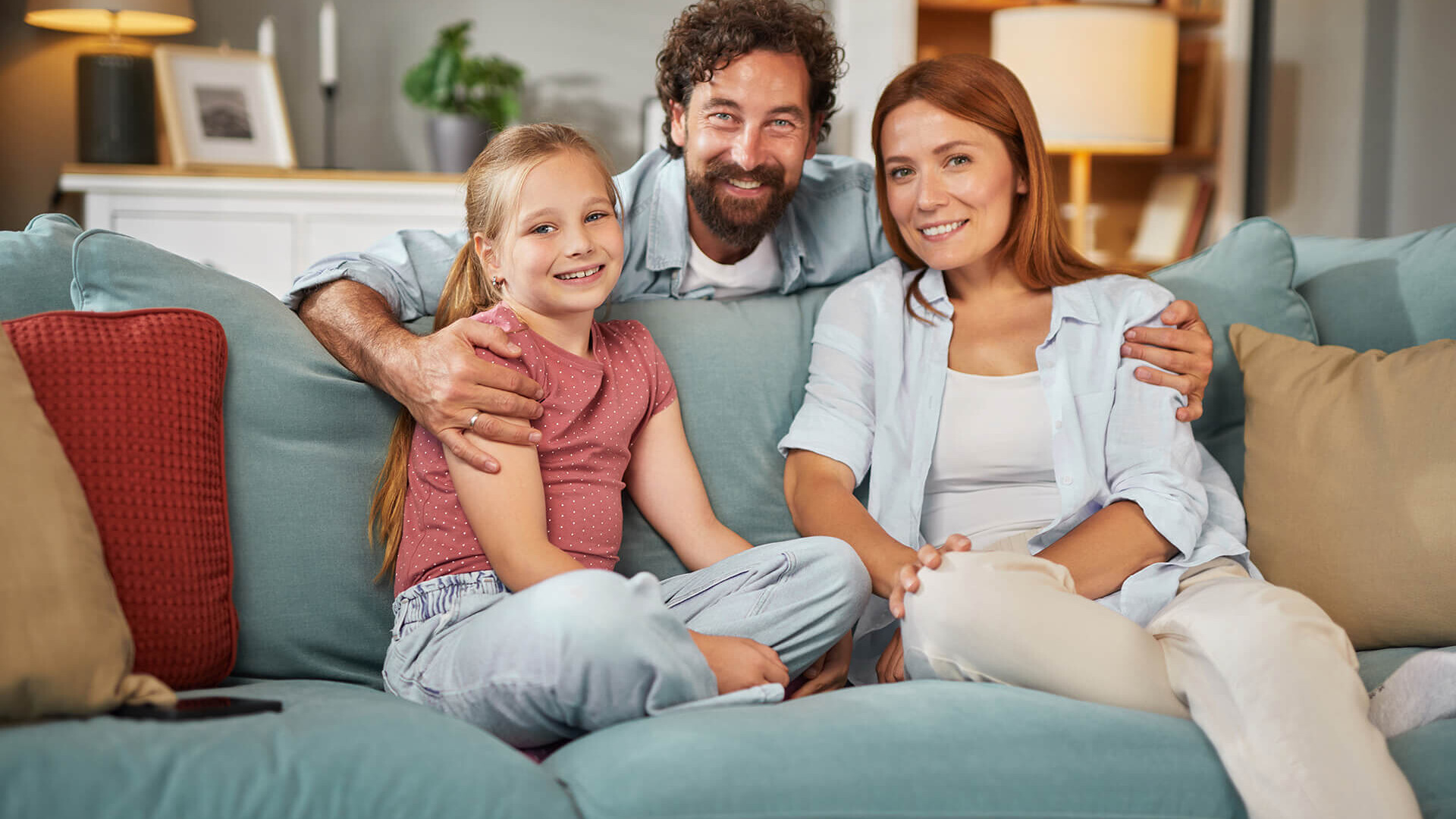 Familie zu dritt auf blauem Sofa im gemütlichen Wohnzimmer