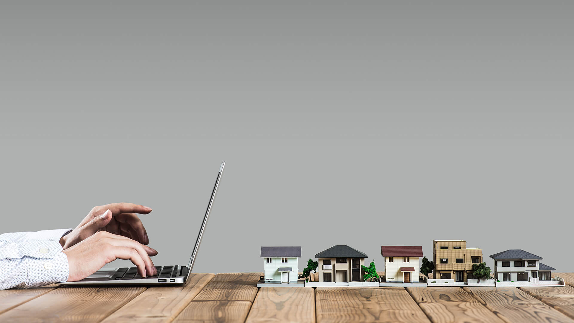 Hände tippen auf Laptop neben Miniaturhäusern auf Holztisch