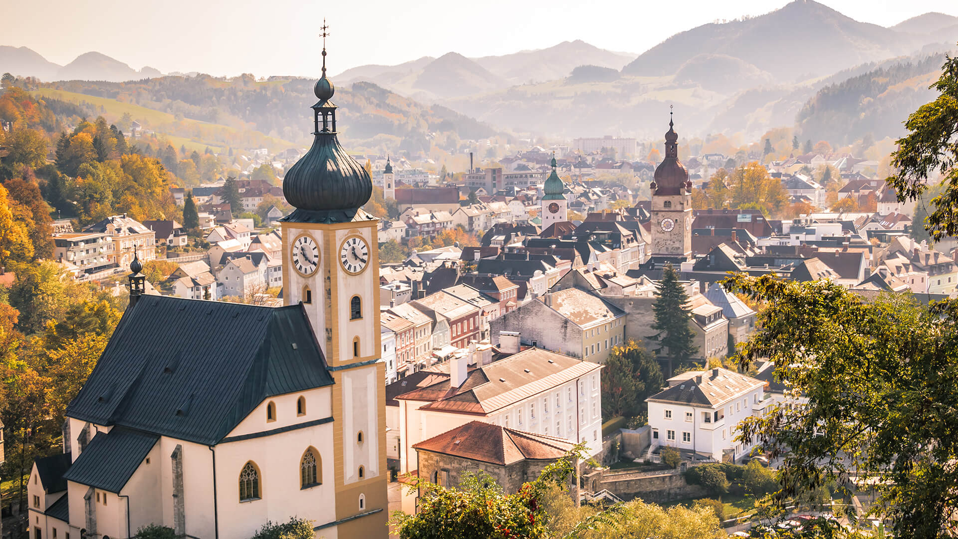 Herbstliche Stadt mit Kirchtürmen zwischen Hügeln und Bäumen