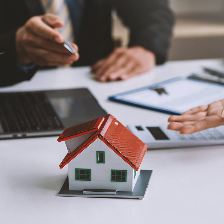 Zwei Personen besprechen Immobilien mit Modellhaus und Laptop