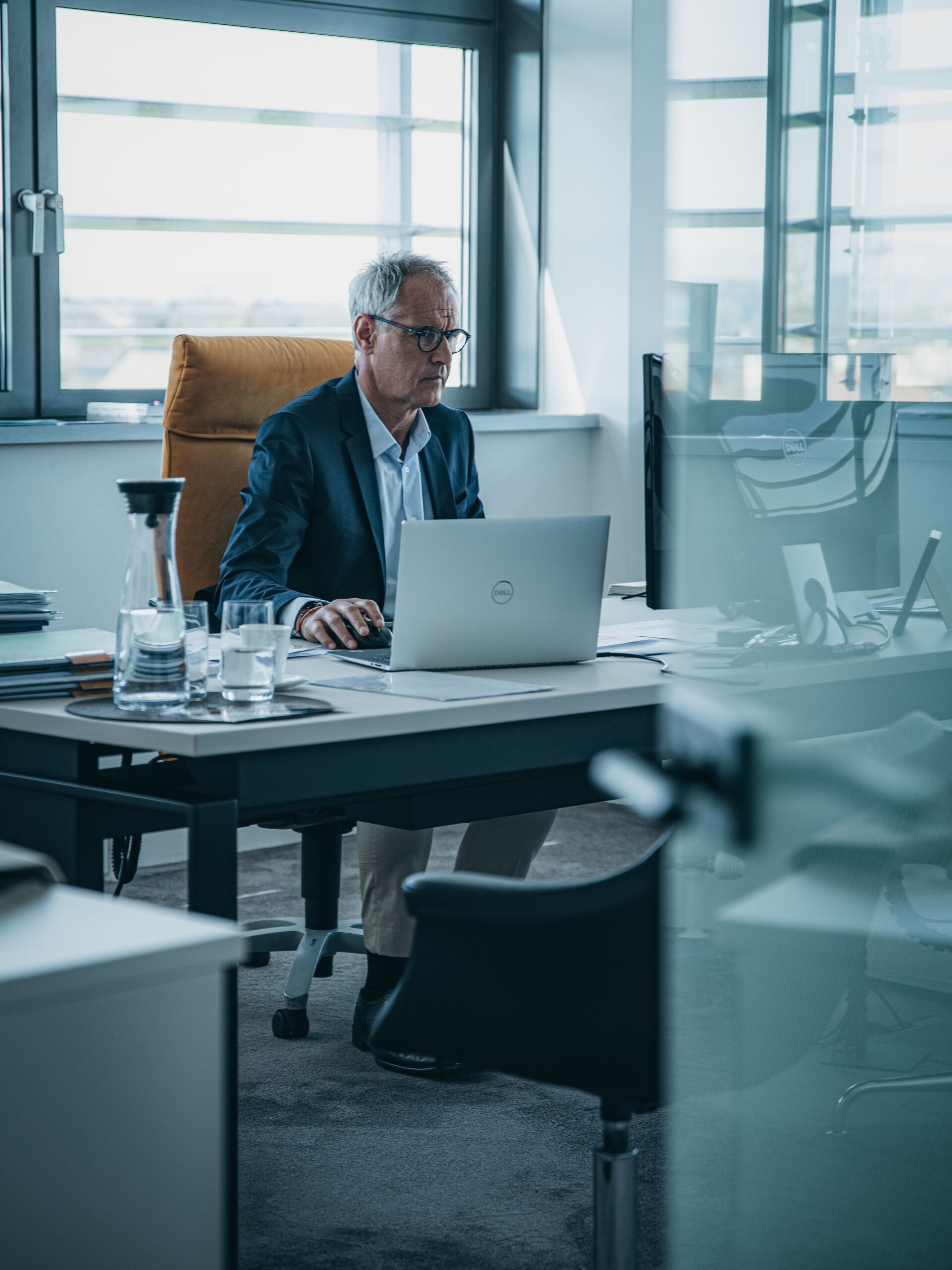 Älterer Mann im Anzug arbeitet am Laptop in modernem Büro