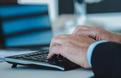 Hände tippen auf Tastatur, verschwommener Laptop im Hintergrund