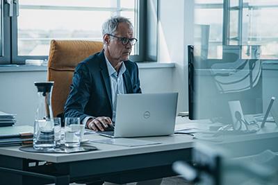 Älterer Mann im Anzug arbeitet am Laptop im modernen Büro
