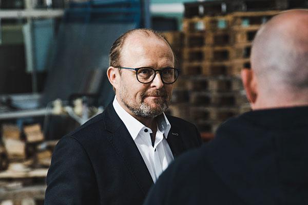 Mann mit Brille und Anzug spricht in einer Lagerhalle mit Person