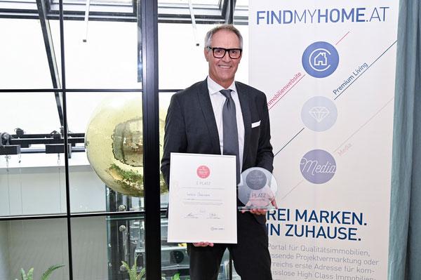 Mann im Anzug mit Auszeichnung vor FindMyHome.at-Banner