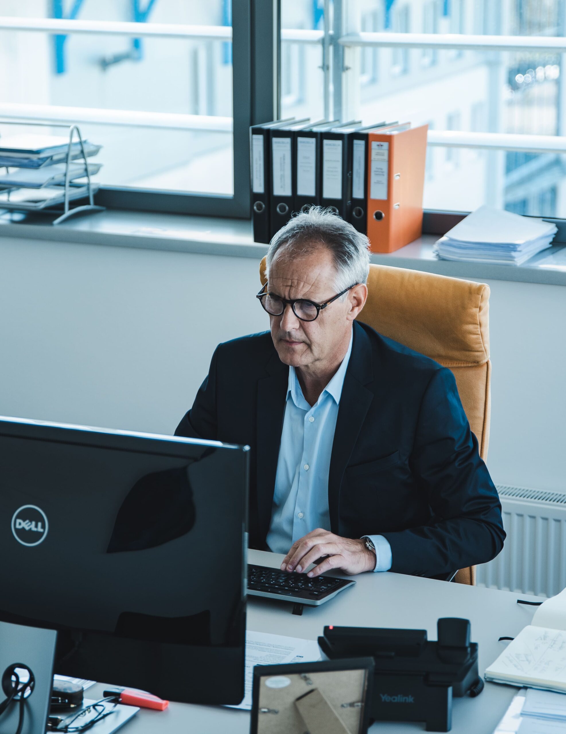 Älterer Mann mit Anzug und Brille arbeitet am Computer in modernem Büro.