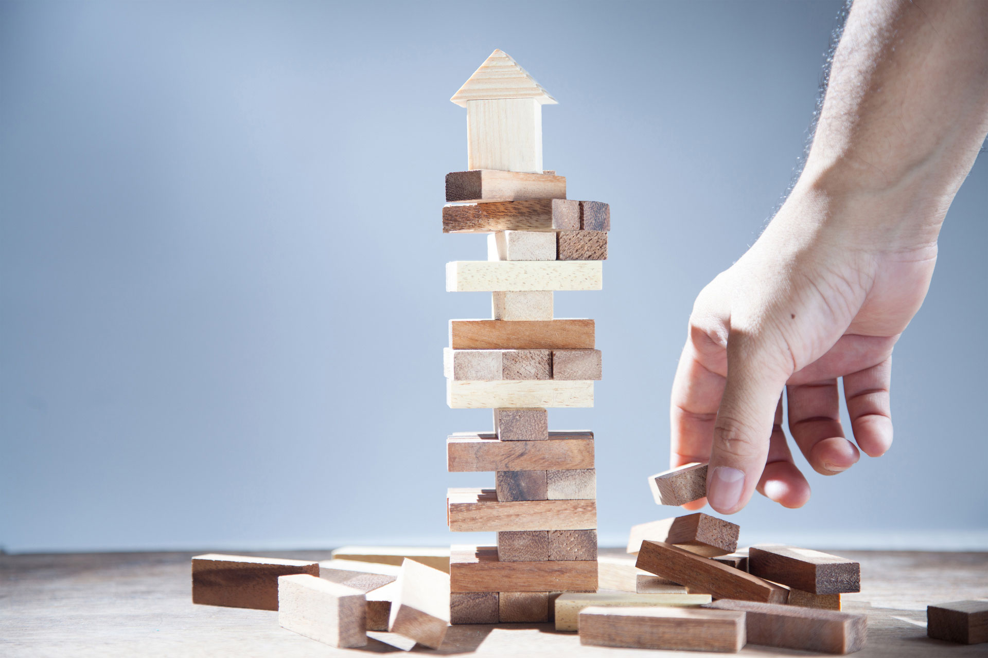 Hand neben gestapelten Jenga-Steinen, auf denen ein Modellhaus steht