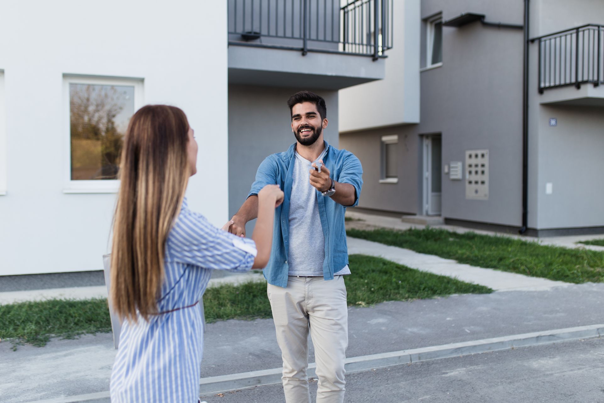 Mann und Frau lächeln, grüßen vor einem modernen Wohnhaus.