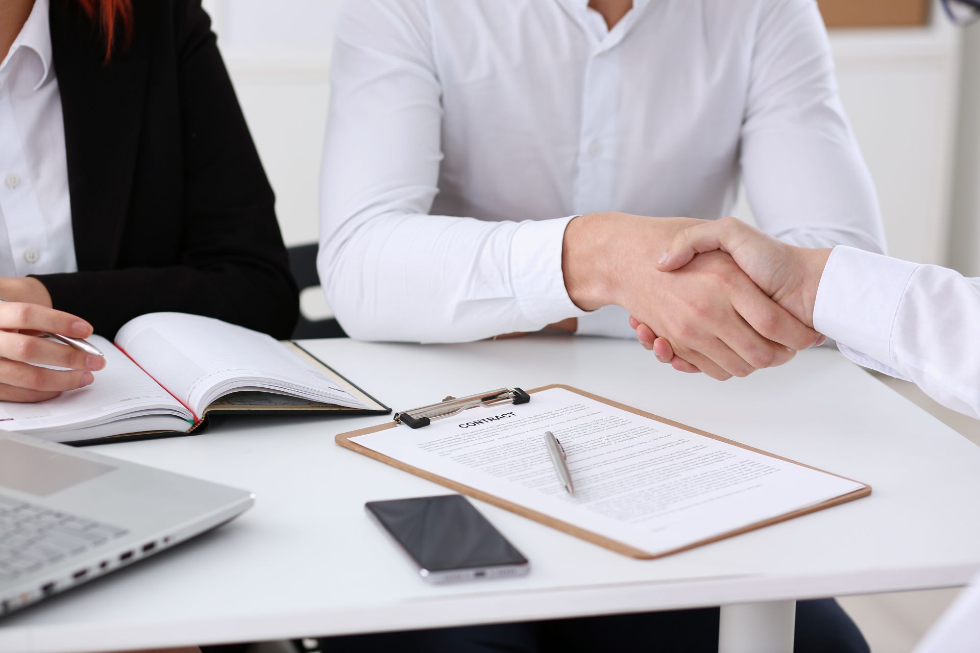 Zwei Personen geben sich am Schreibtisch die Hand, Vertrag liegt da.