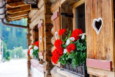 Traditionelle Blockhütte aus Holz mit Herz-Fensterläden und roten Geranien.