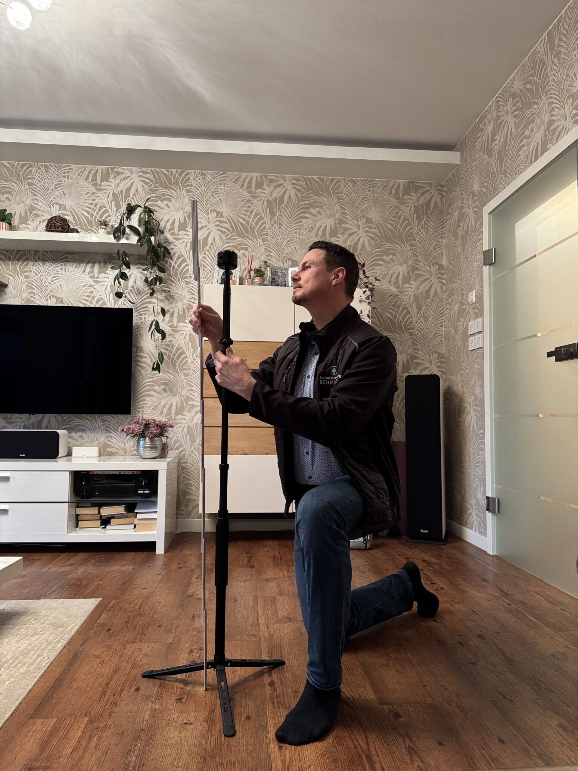 Mann kniet am Holzfußboden, richtet Ständer im Wohnzimmer aus.