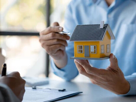 Person hält Modellhaus, andere unterschreibt Vertrag, Immobilien.