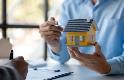 Zwei Personen mit Modellhaus und Dokumenten bei Immobilienkauf.