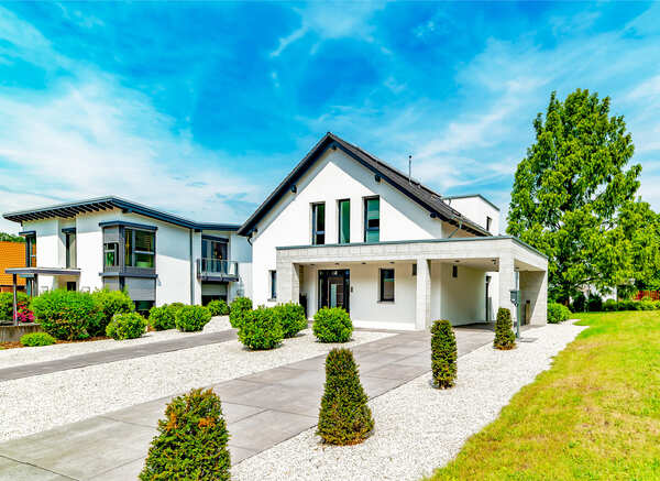 Weißes Haus mit Einfahrt, Sträuchern und blauem Himmel.
