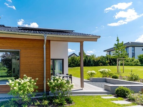Modernes Haus mit Holzverkleidung, Terrasse, Blumen und grünem Rasen.