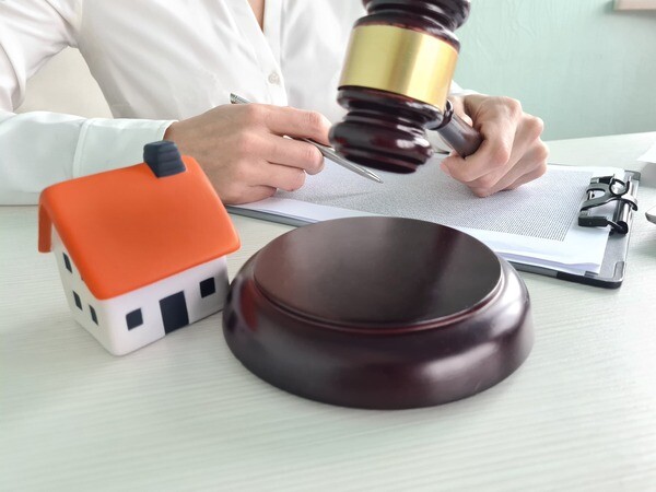 Person unterschreibt neben Richterhammer und kleinem Hausmodell.