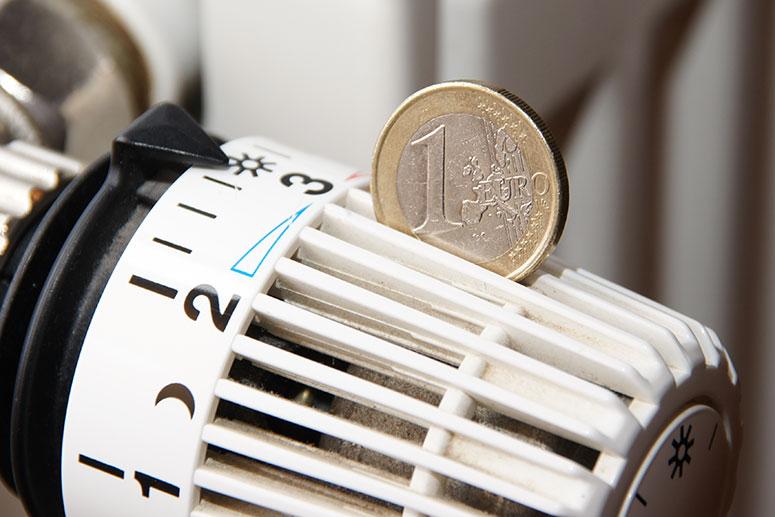 Nahaufnahme eines Thermostats mit einer 1-Euro-Münze darauf, symbolisiert Heizkosten oder Energiesparen.