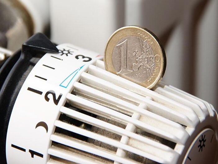 Nahaufnahme eines Thermostats mit einer 1-Euro-Münze darauf, symbolisiert Heizkosten oder Energiesparen.