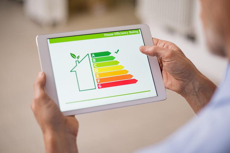 Nahaufnahme eines Mannes, der ein Tablet hält, das einen "House Efficiency Rating"-Bildschirm mit einem Energiesparkonzept und einer Skala von A bis G anzeigt.