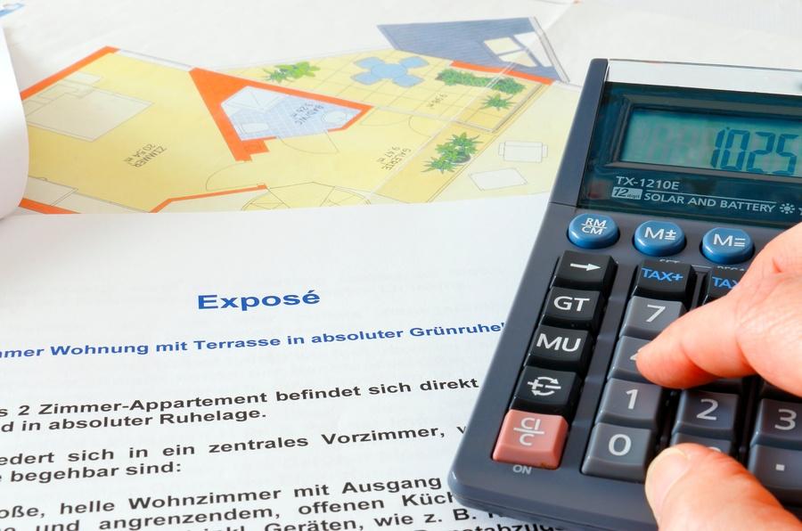 Hand tippt auf einem Taschenrechner vor einem Exposé und einem Grundriss.