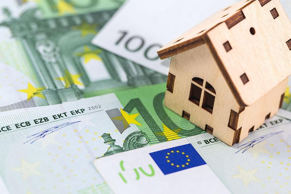 Ein kleines Holzhausmodell steht auf ausgebreiteten 100-Euro-Banknoten.