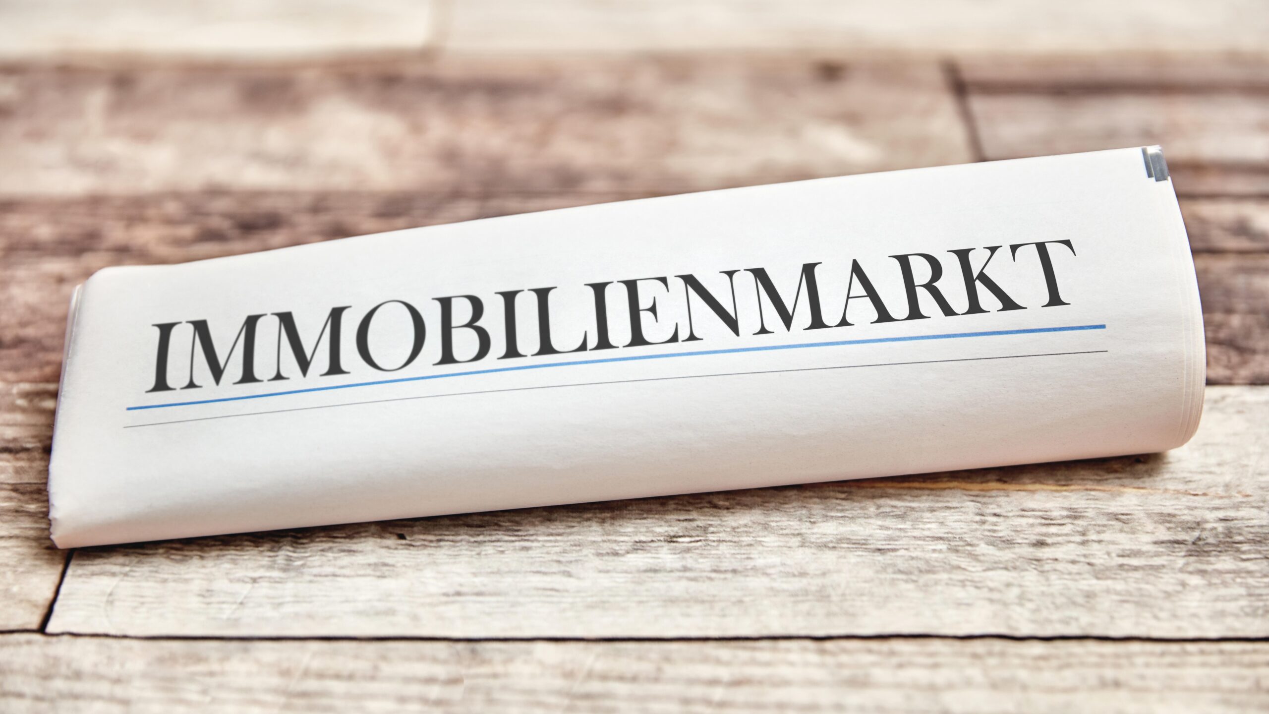 Ein Zeitungsartikel mit der Überschrift "IMMOBILIENMARKT" liegt auf einer Holzoberfläche.