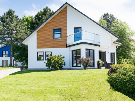 Modernes Einfamilienhaus mit weißer Fassade und Holzverkleidung, Balkon und großem Garten