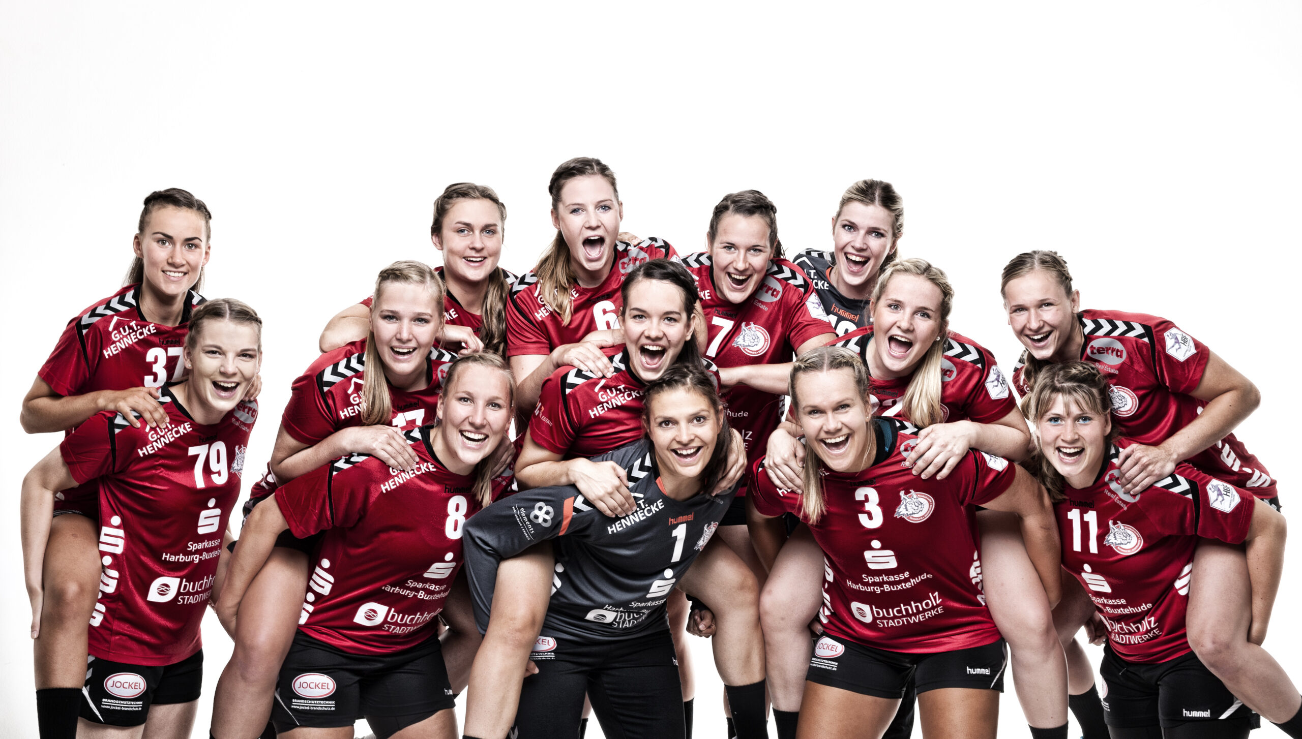 Frauen-Handballmannschaft in roten Trikots posiert lachend und eng zusammen für ein Teamfoto