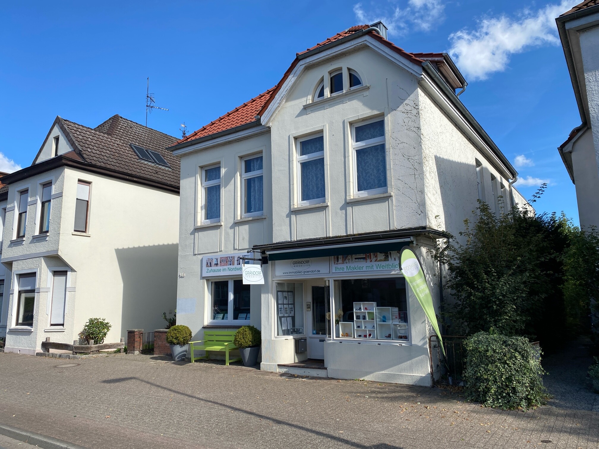 Weißes Gebäude mit Laden unten und Wohnungen oben, blauer Himmel.