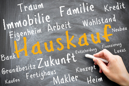 Hand schreibt "Hauskauf" auf Tafel mit Begriffen zum Hauskauf.