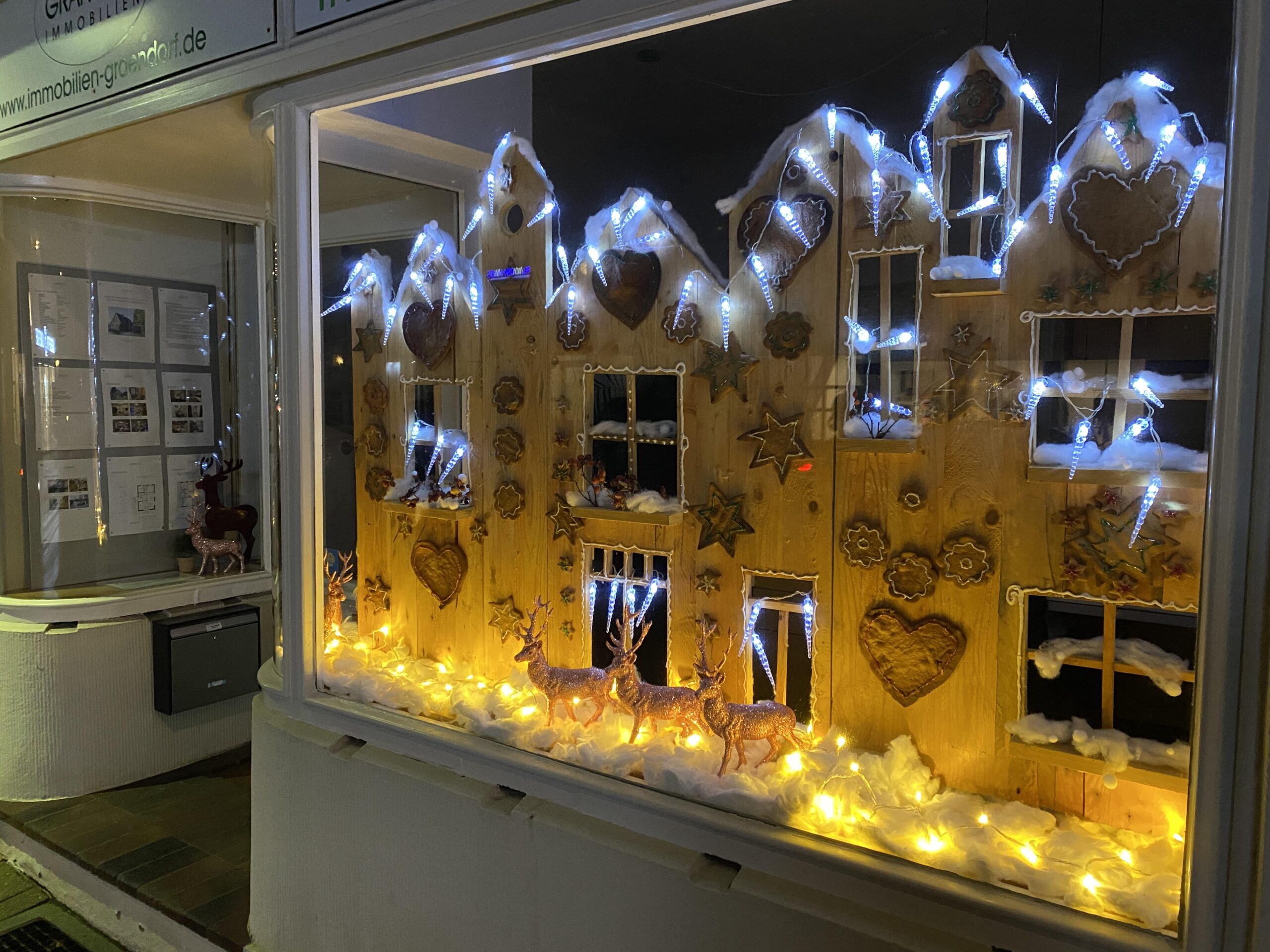 Beleuchtete Holz-Weihnachtslandschaft mit Rentieren im Schaufenster.