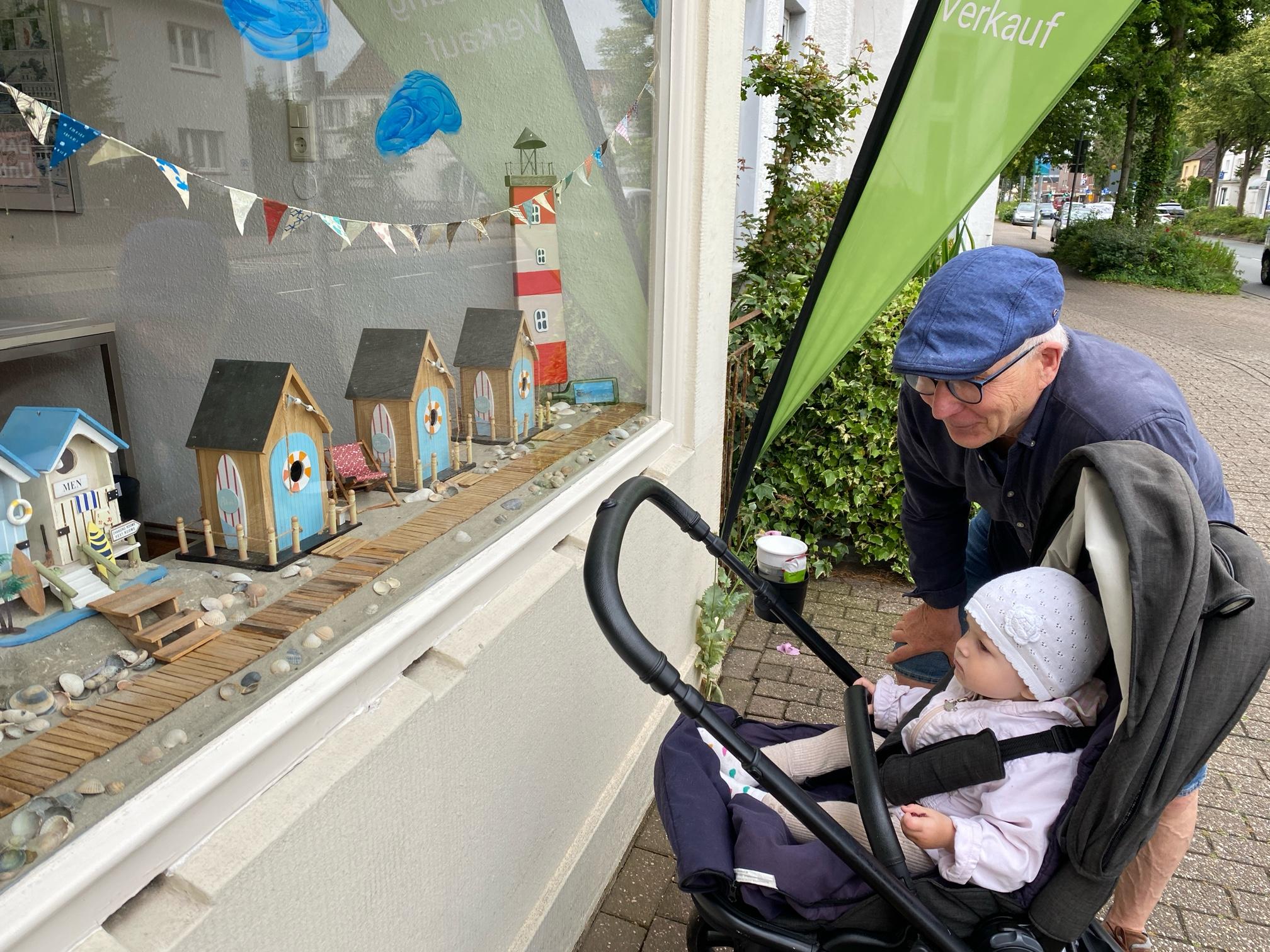 Älterer Mann mit Baby betrachtet maritimen Schaufensterdeko.