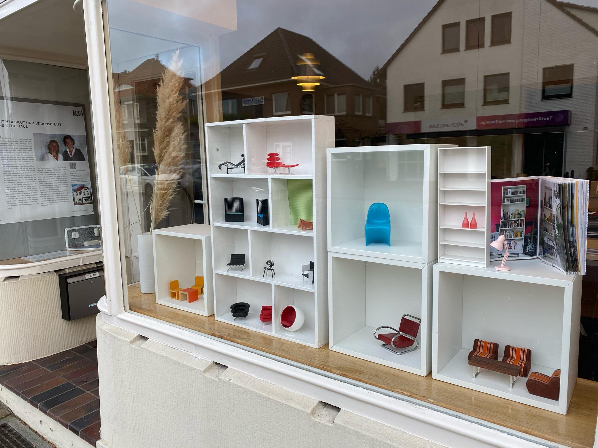 Moderne Miniaturmöbel in weißen Würfelregalen im Schaufenster.