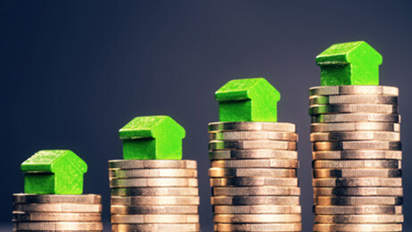 Münzstapel mit kleinen grünen Häusern, ansteigend von links nach rechts.