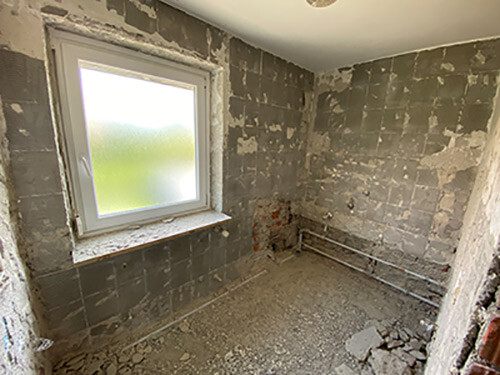 Unfertiger Raum mit Putz, Fliesen, blankem Boden und Milchglasfenster.