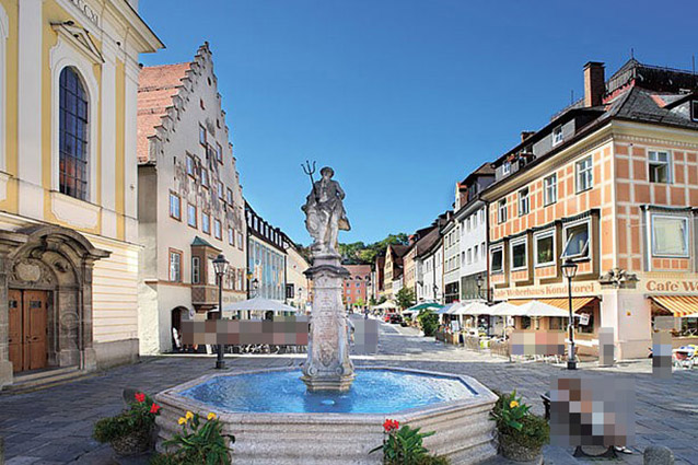 Springbrunnen mit Statue auf dem Europaplatz, bunte Gebäude in der Nähe.