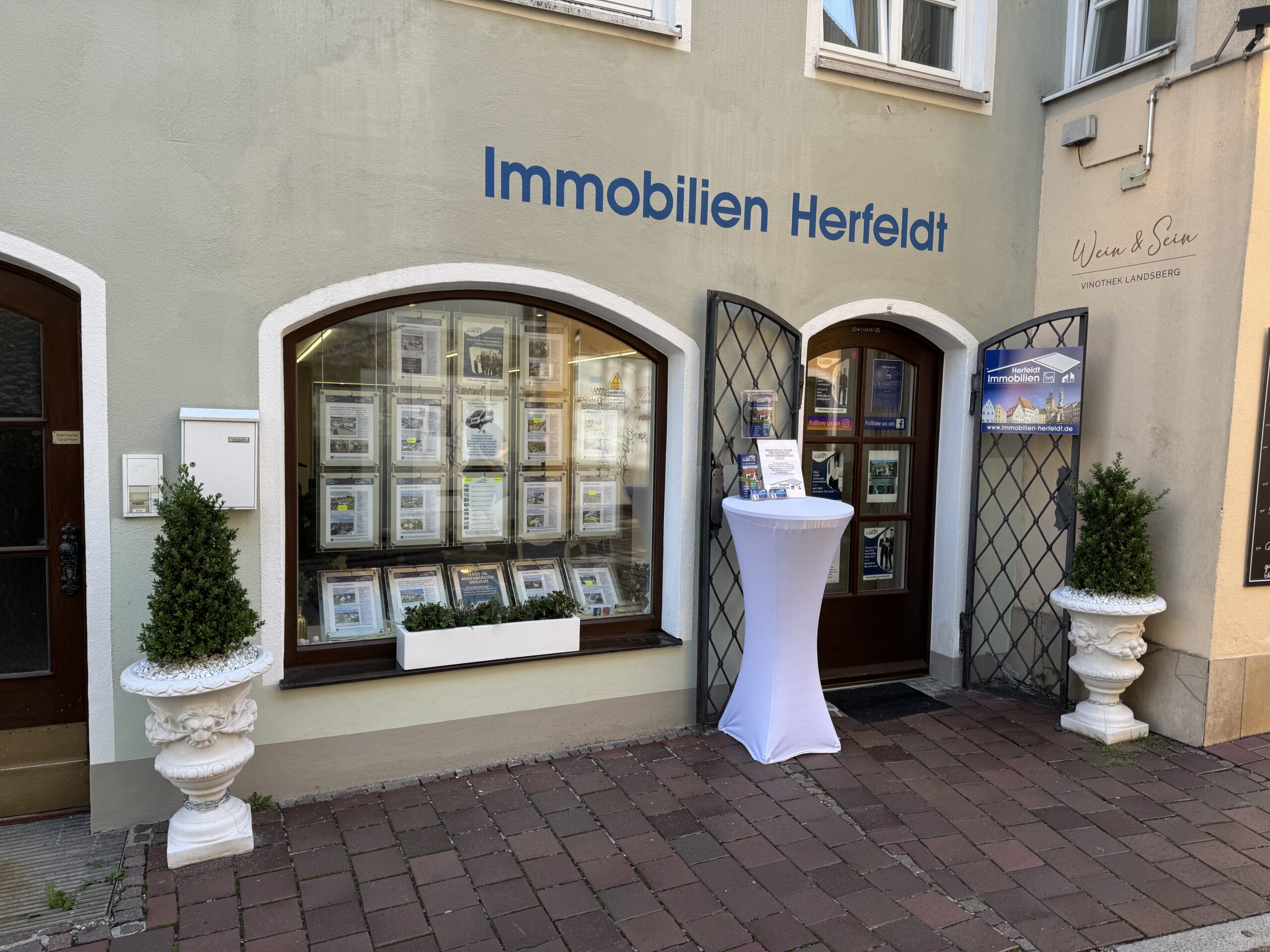 Immobilien Herfeldt Schaufenster mit Fensterdeko, weißer Stehtisch.