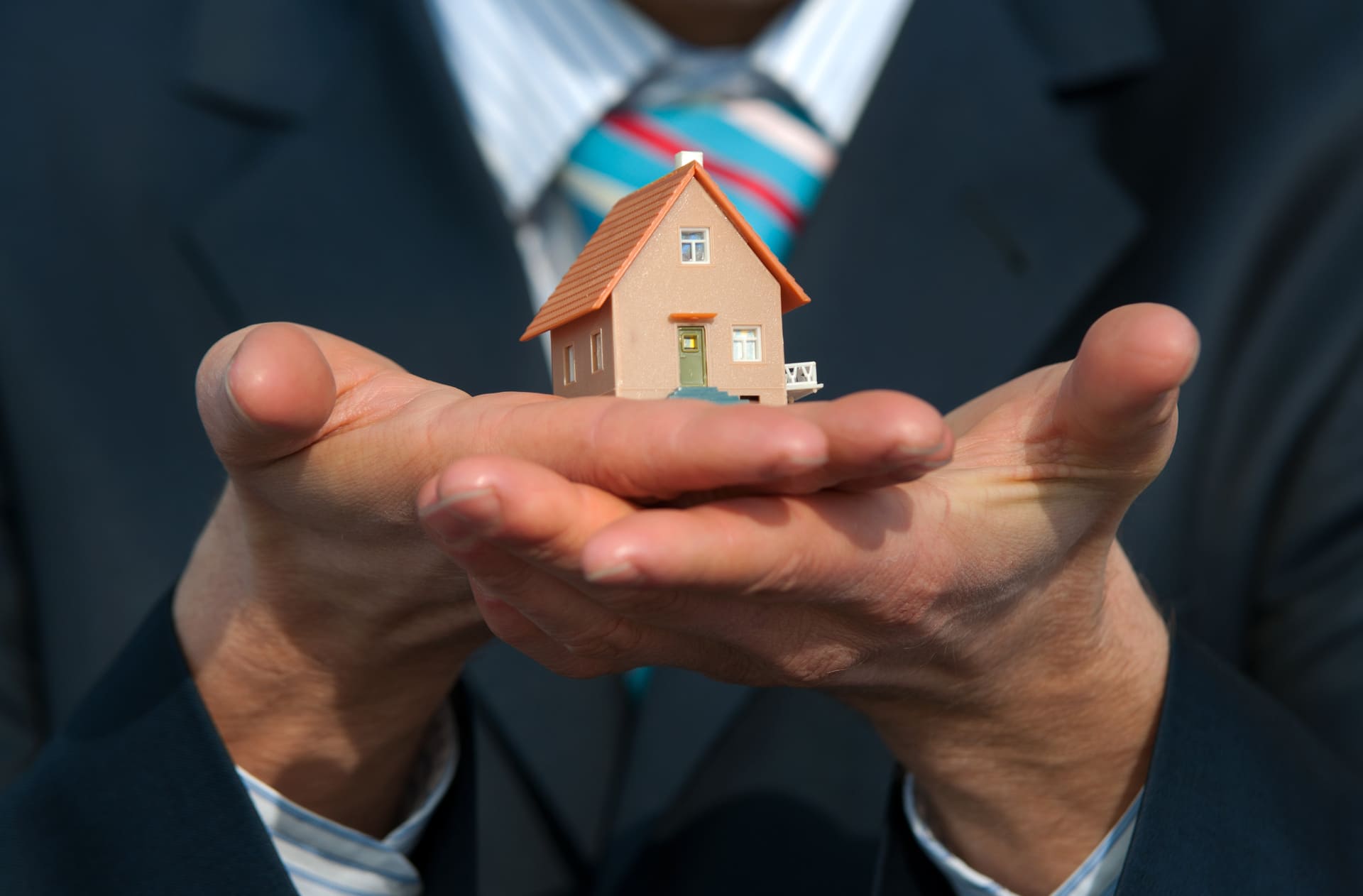 Mann im Anzug hält ein Modellhaus in die Kamera.