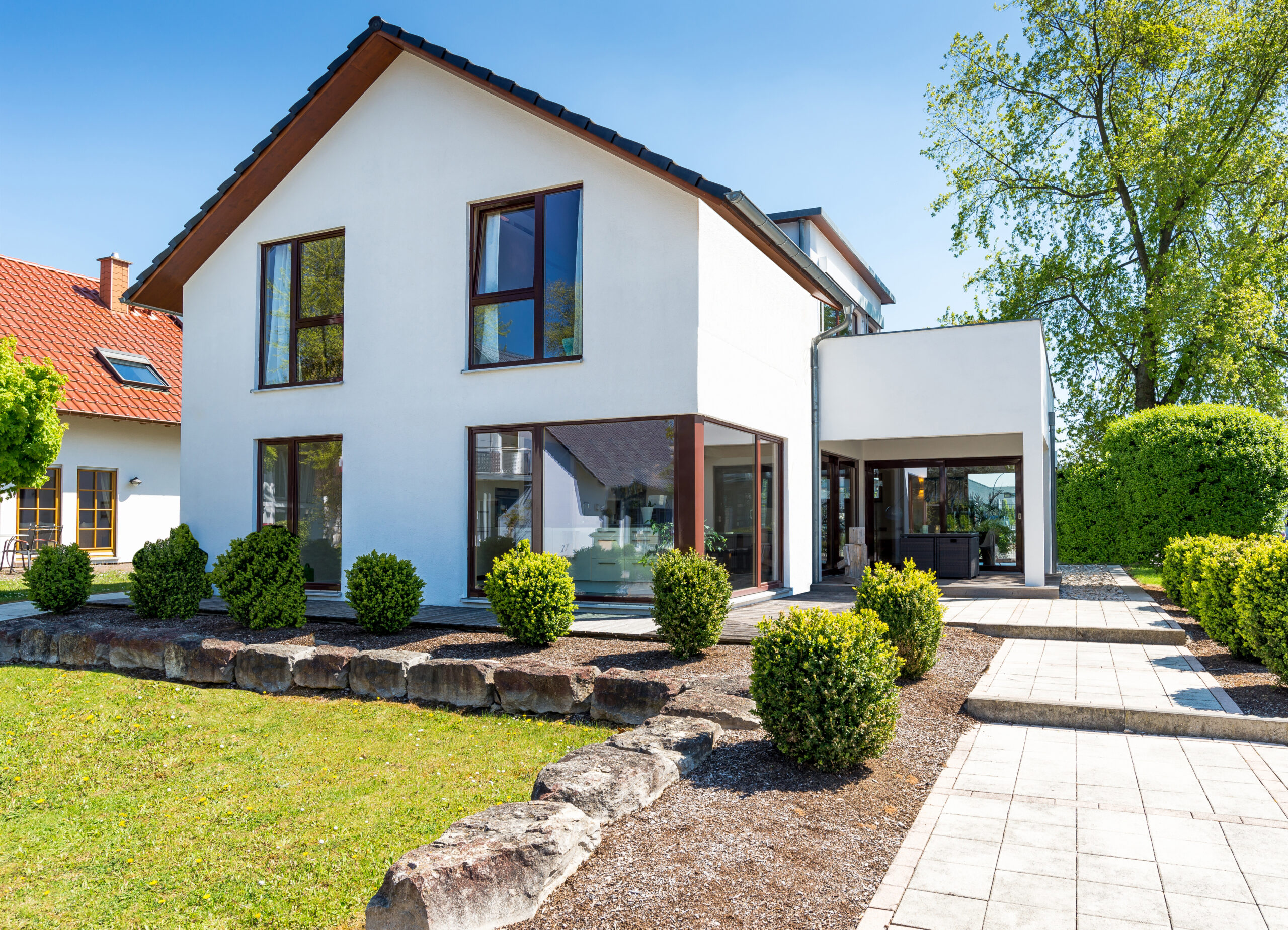 Weißes Haus mit großen Fenstern und gepflegtem Garten bei Sonne.