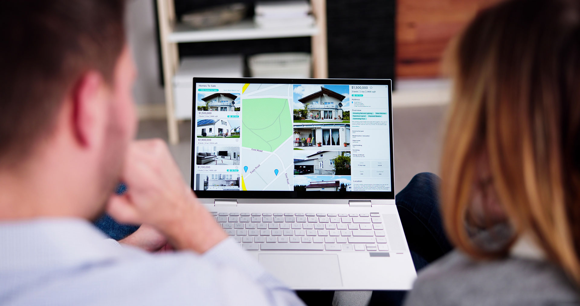 Zwei Personen sehen sich Immobilien auf einem Laptop im Wohnzimmer an.