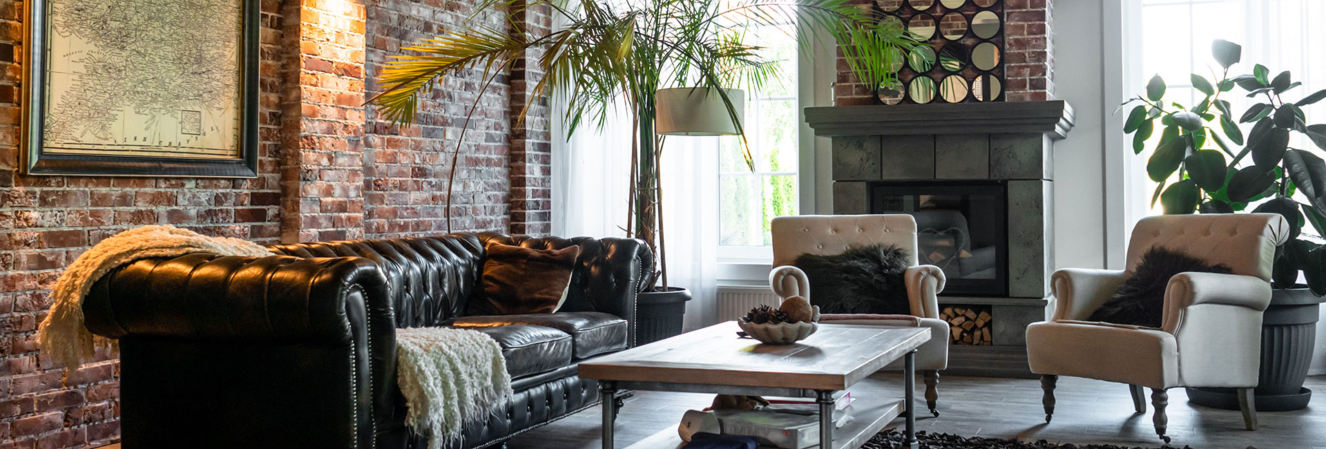 Wohnzimmer mit Backsteinwand, Ledersofa, Sesseln, Pflanzen, Kamin.