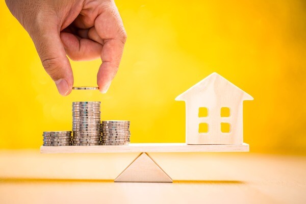 Waage mit Modellhaus und Münzen