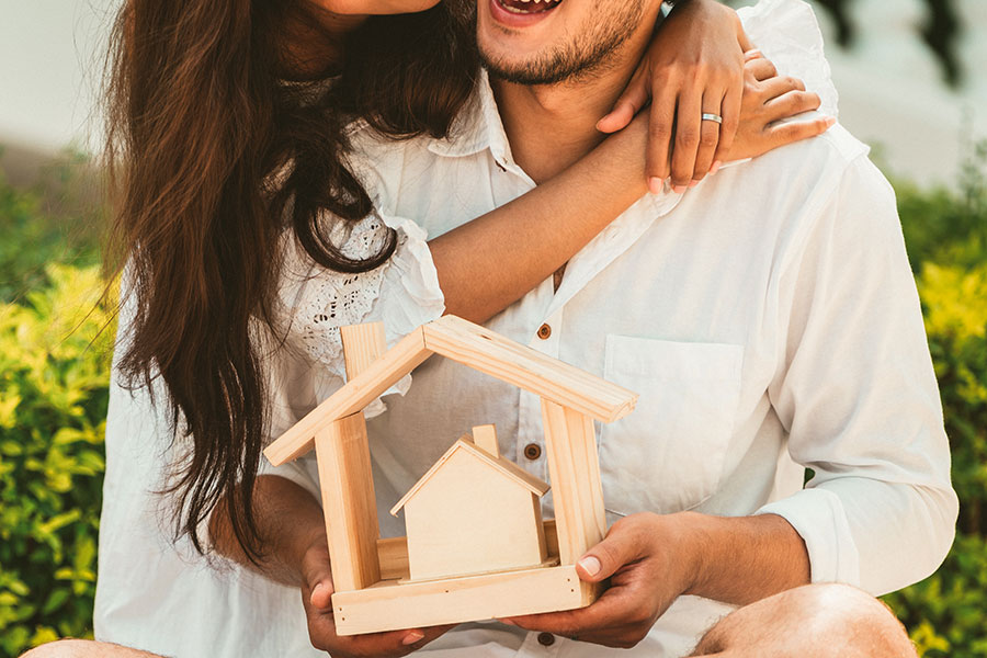 Pärchen umarmt sich und hält Modellhaus aus Holz in der Hand.